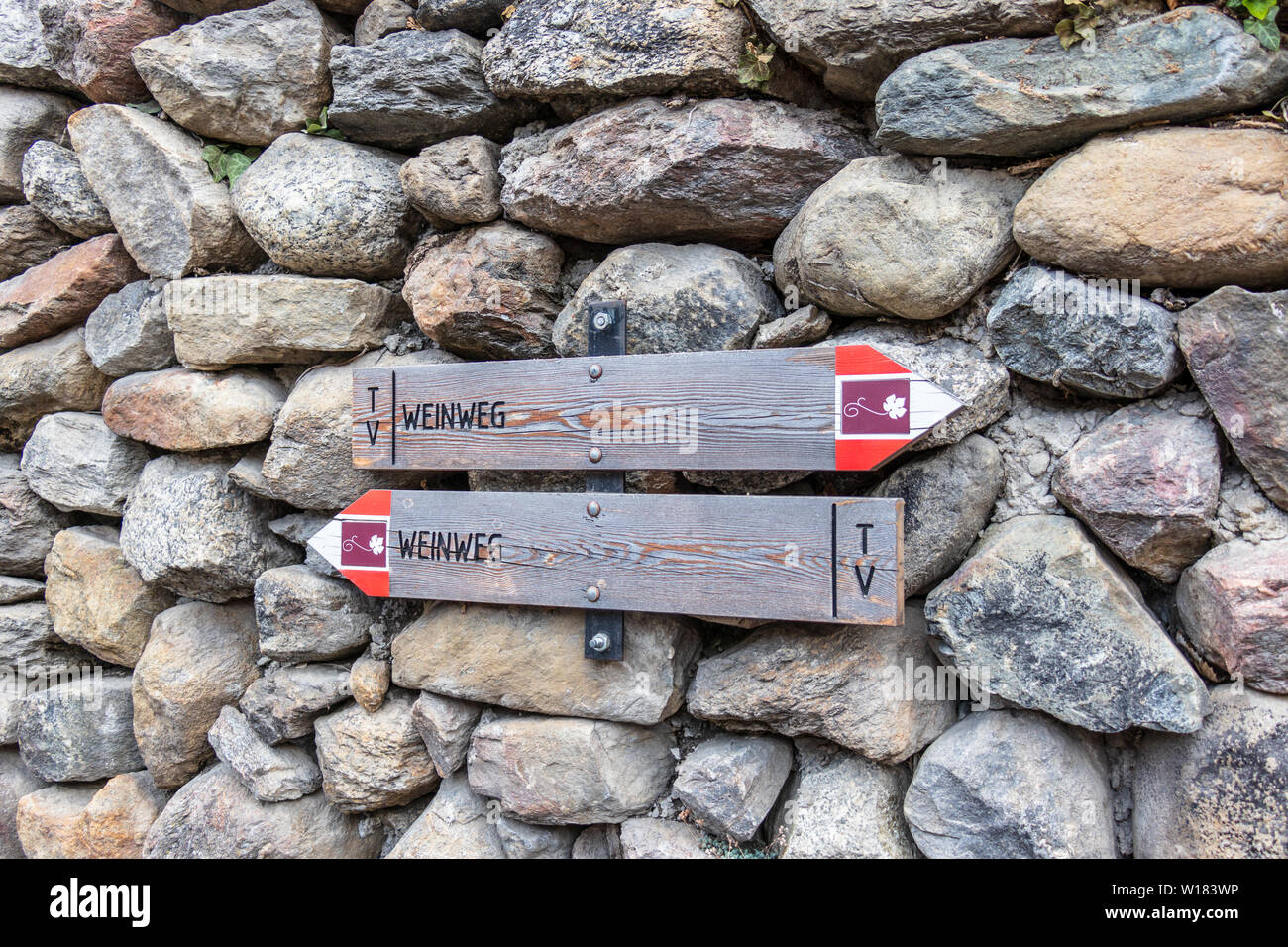Due indicazioni su un stonewall guidare gli escursionisti alla Strada del Vino, in tedesco, Weinweg, in Alto Adige. Foto Stock