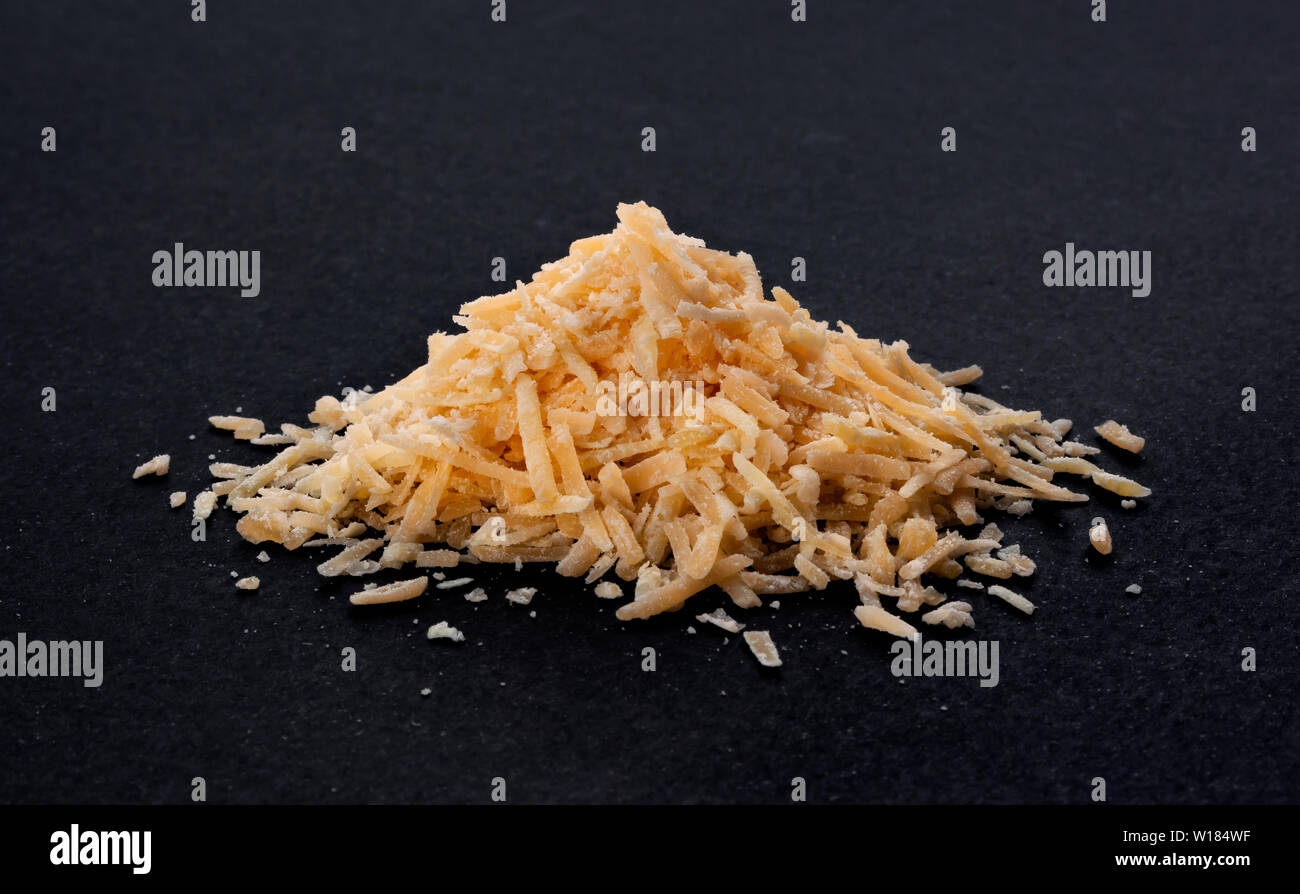 Pila di formaggio grattugiato su sfondo nero Foto Stock