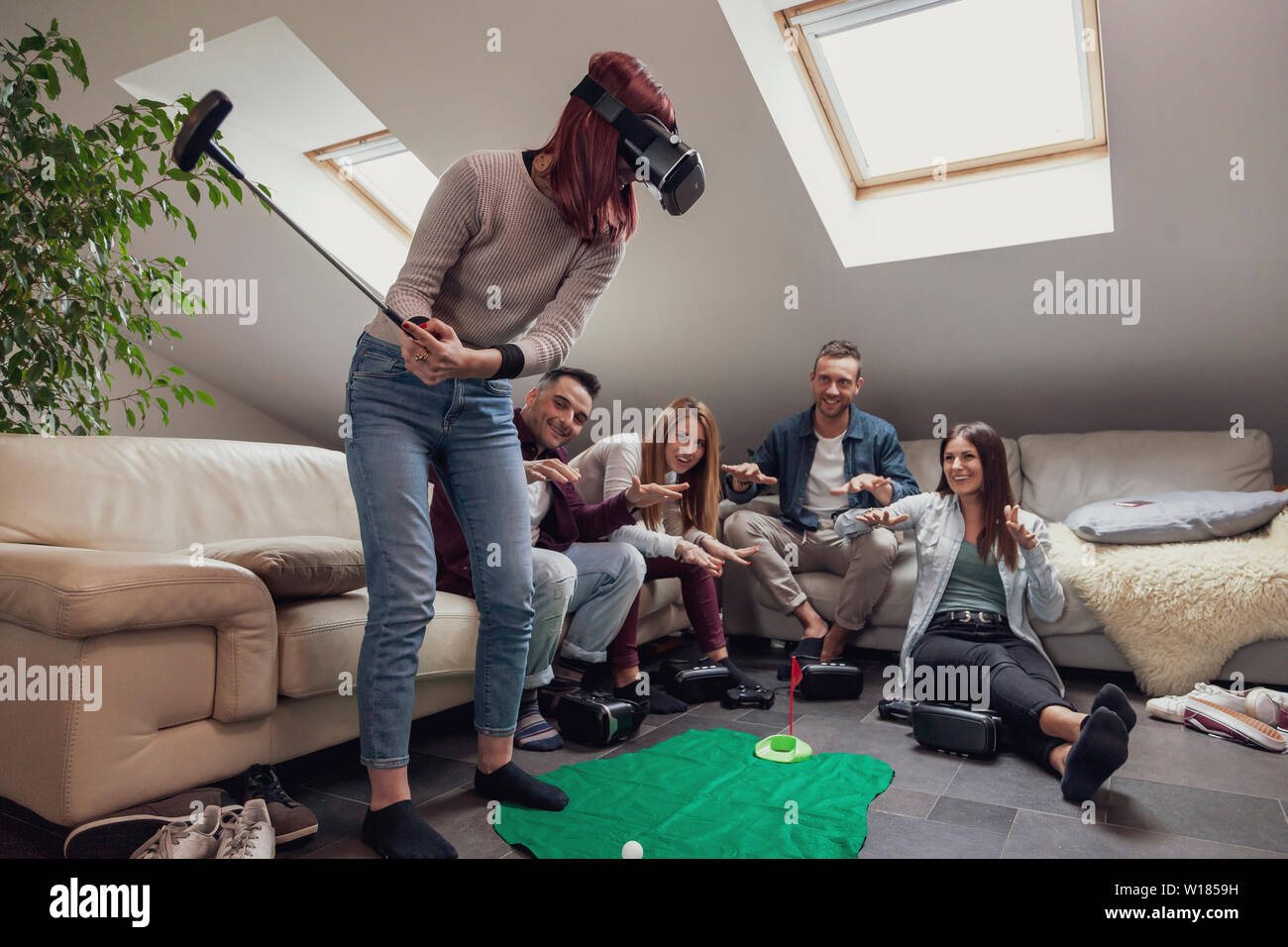 Un gruppo di giovani adulti divertirsi giocando a golf con video giochi occhiali per realtà virtuale nella stanza vivente Foto Stock