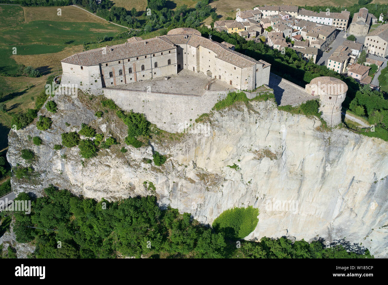 VISTA AEREA. Fortezza medievale in piedi su un mesa isolato. San Leo, Provincia di Rimini, Emilia-Romagna, Italia. Foto Stock