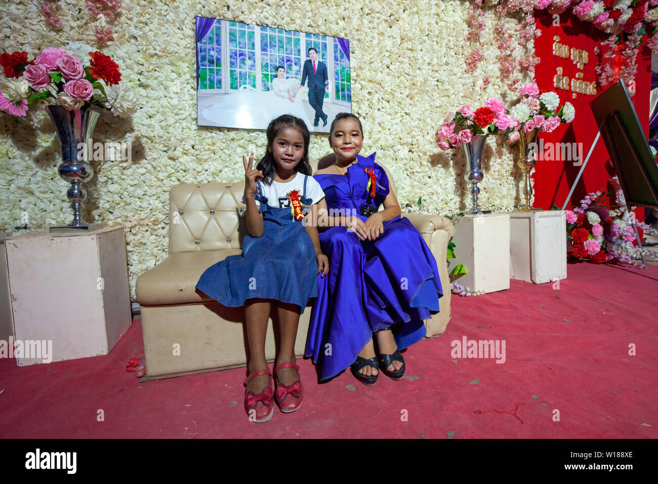 Due giovani ragazze cambogiane posano per una foto sotto una fotografia raffigurante la sposa e lo sposo a Khmer cerimonia di nozze in Siem Reap, Cambogia. Foto Stock