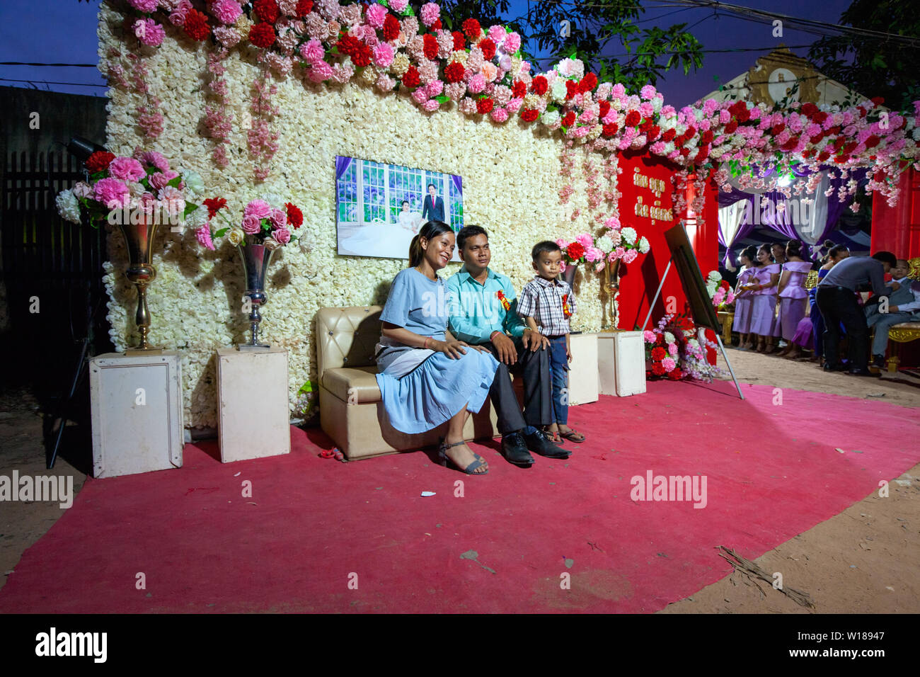 Un cambogiano di famiglia in posa per una foto sotto una fotografia raffigurante la sposa e lo sposo a Khmer tradizionale cerimonia di matrimonio in Siem Reap, Cambogia. Foto Stock