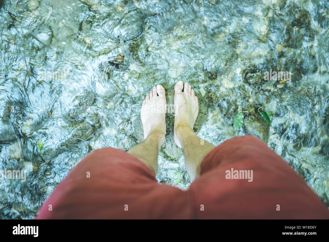Tagliare dei maschi di piedi scalzi con pantaloni rossi a piedi in un fiume poco profondo Foto Stock