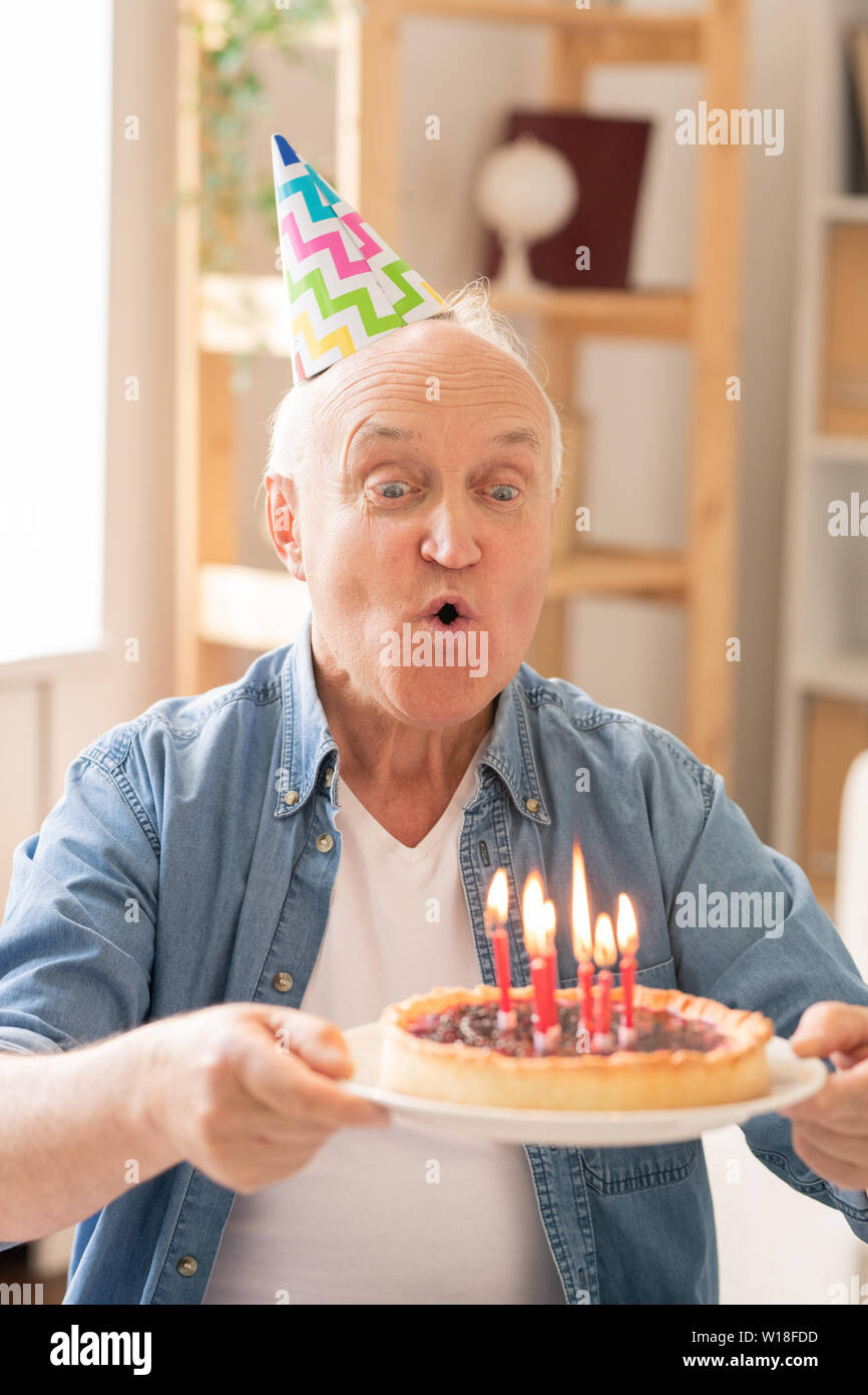 Uomo più anziano soffiando candele sui fatti in casa torta di compleanno mentre si celebra da soli Foto Stock