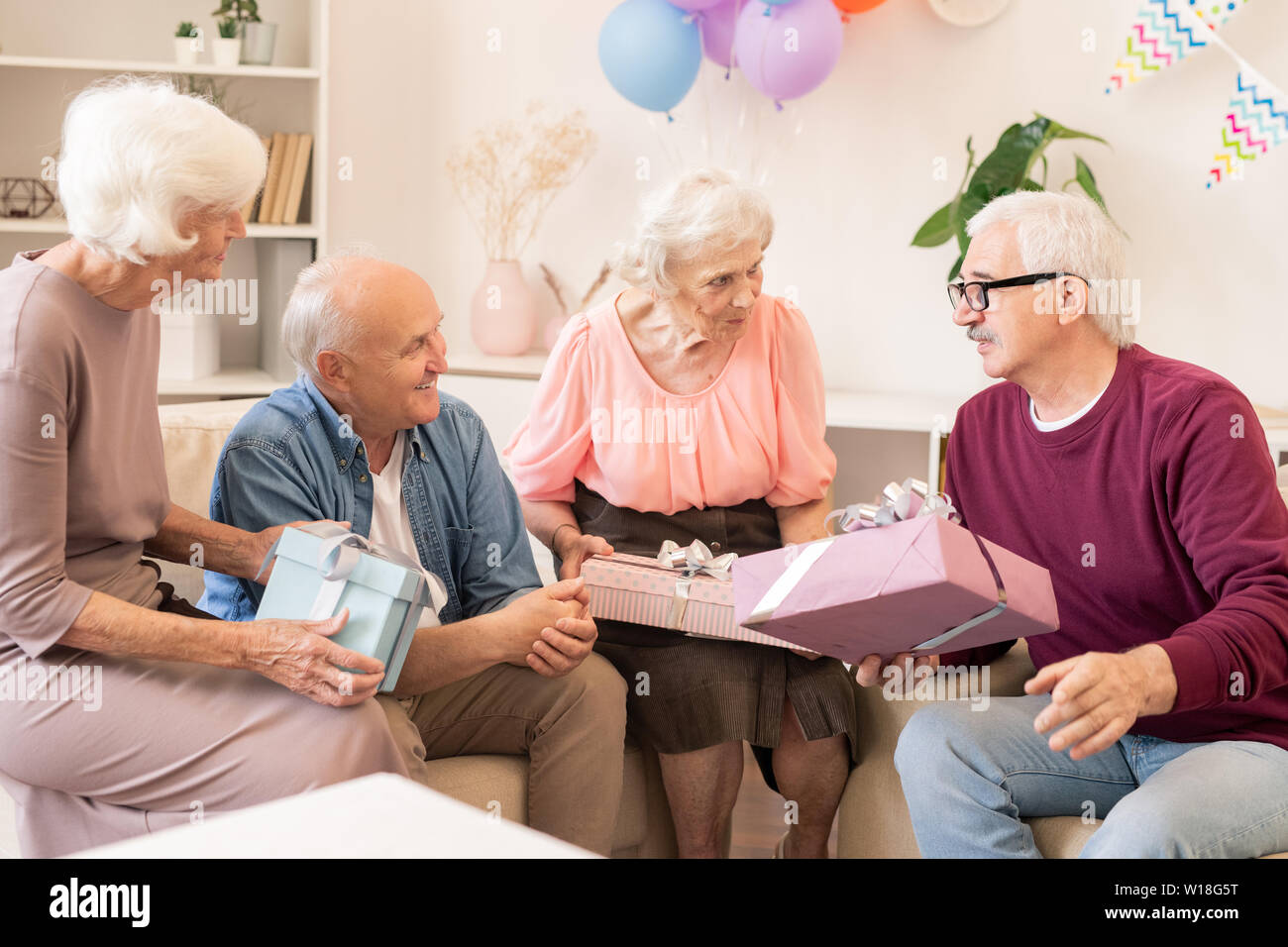 Quattro seniors contemporanea facendo regali gli uni agli altri e parlare durante la celebrazione della vacanza a casa Foto Stock