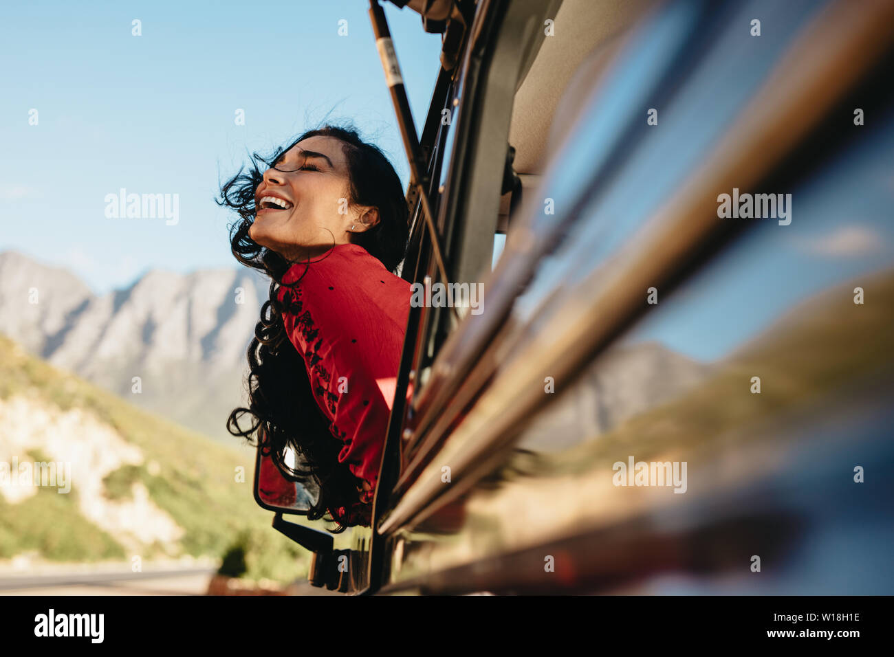 Sorridente giovane donna guardando fuori della vettura con i suoi capelli volare in aria. Donna godendo il giro in macchina in un viaggio su strada. Foto Stock
