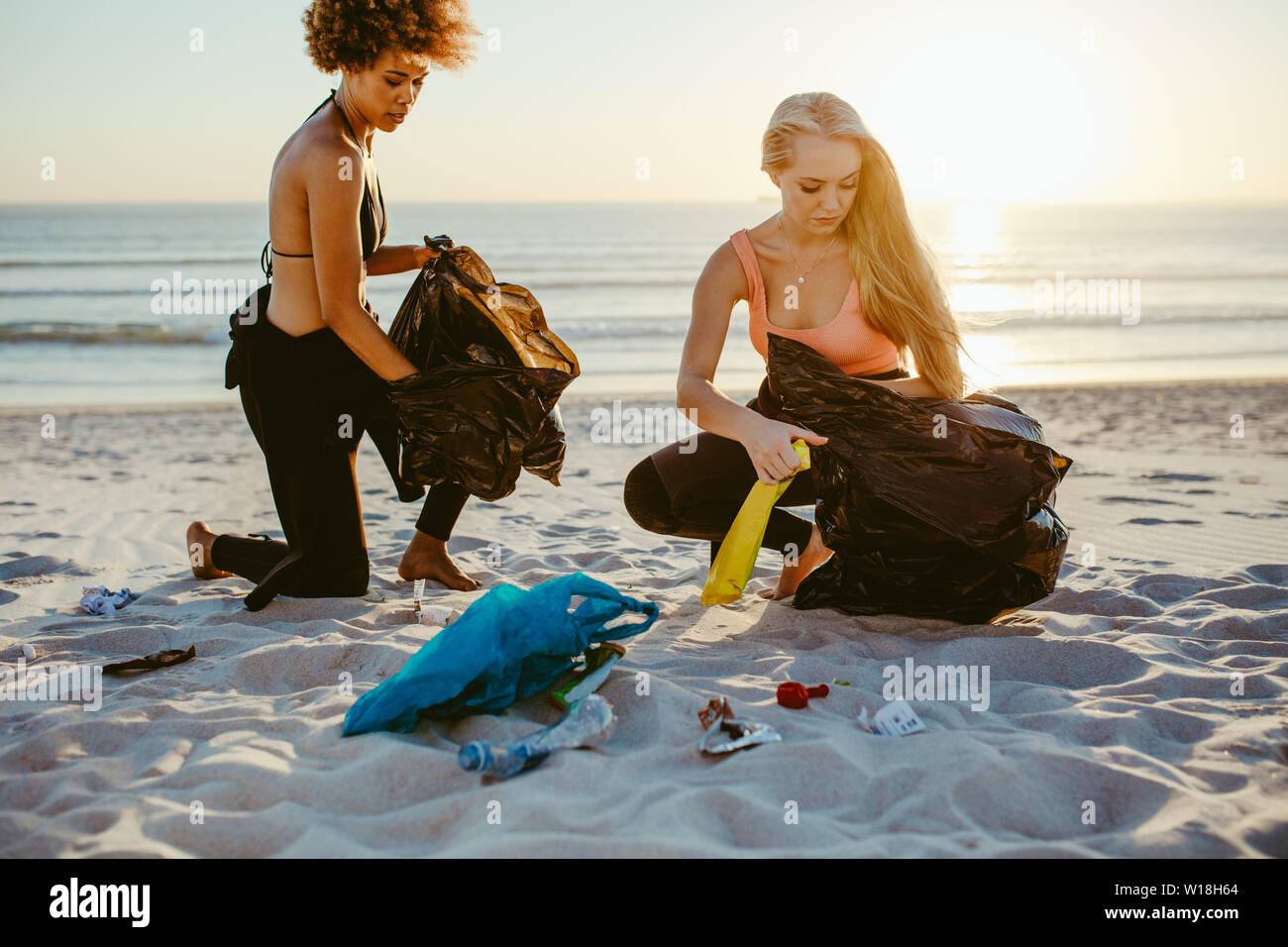 Due femmina surfers prelievo di lettiera sulla spiaggia. Volontari di sesso femminile la pulizia della spiaggia. Foto Stock