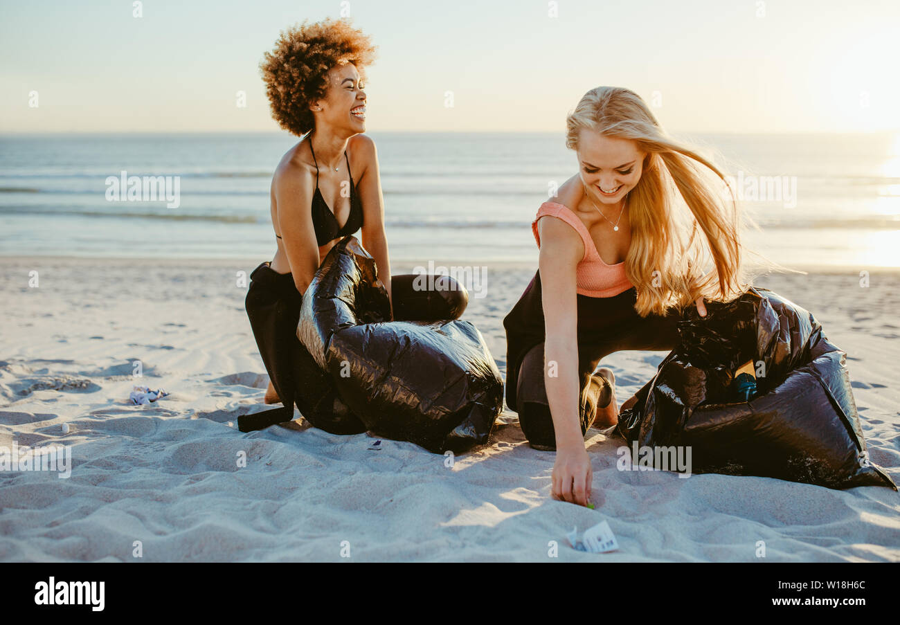 Felice surfisti femmina facendo cestino tag challenge sulla spiaggia. Donne pulizia area di spiaggia. Foto Stock