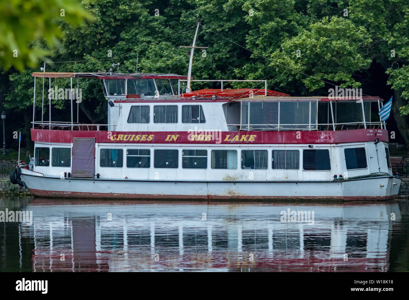 IOANNINA, Grecia - 6 giugno 2019 - abbandonato piccolo vecchio bianco e rosso crociera turistica nave traghetto con due pianali posto barca sul lago Pamvotida vicino alla piccola e bella città greca. Riflessi dell'acqua. Foto Stock