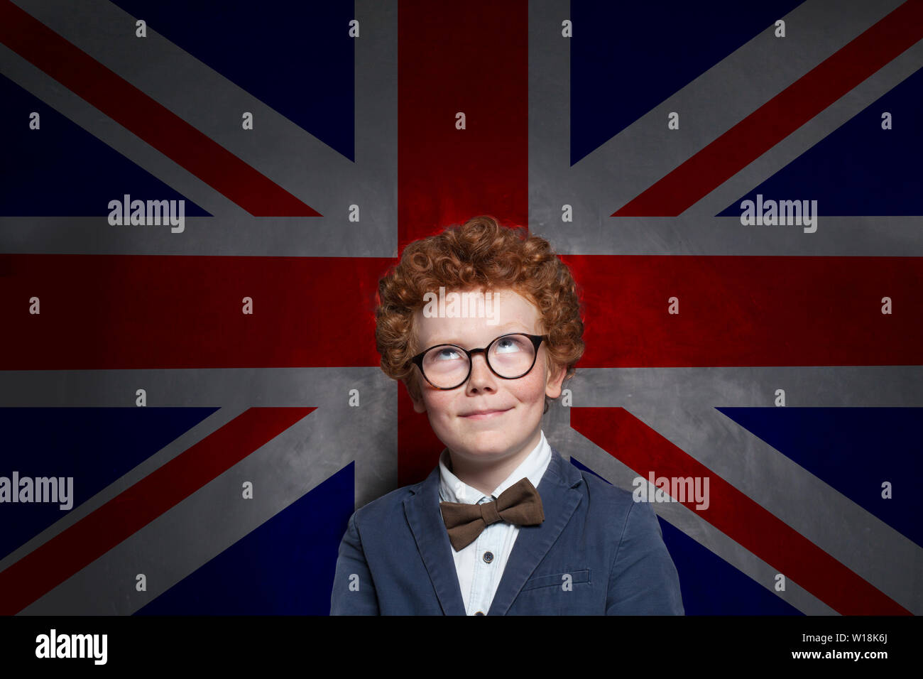 Bambino felice ragazzo inglese studen cercando sulla bandiera del Regno Unito lo sfondo. Impara Inglese Concept Foto Stock