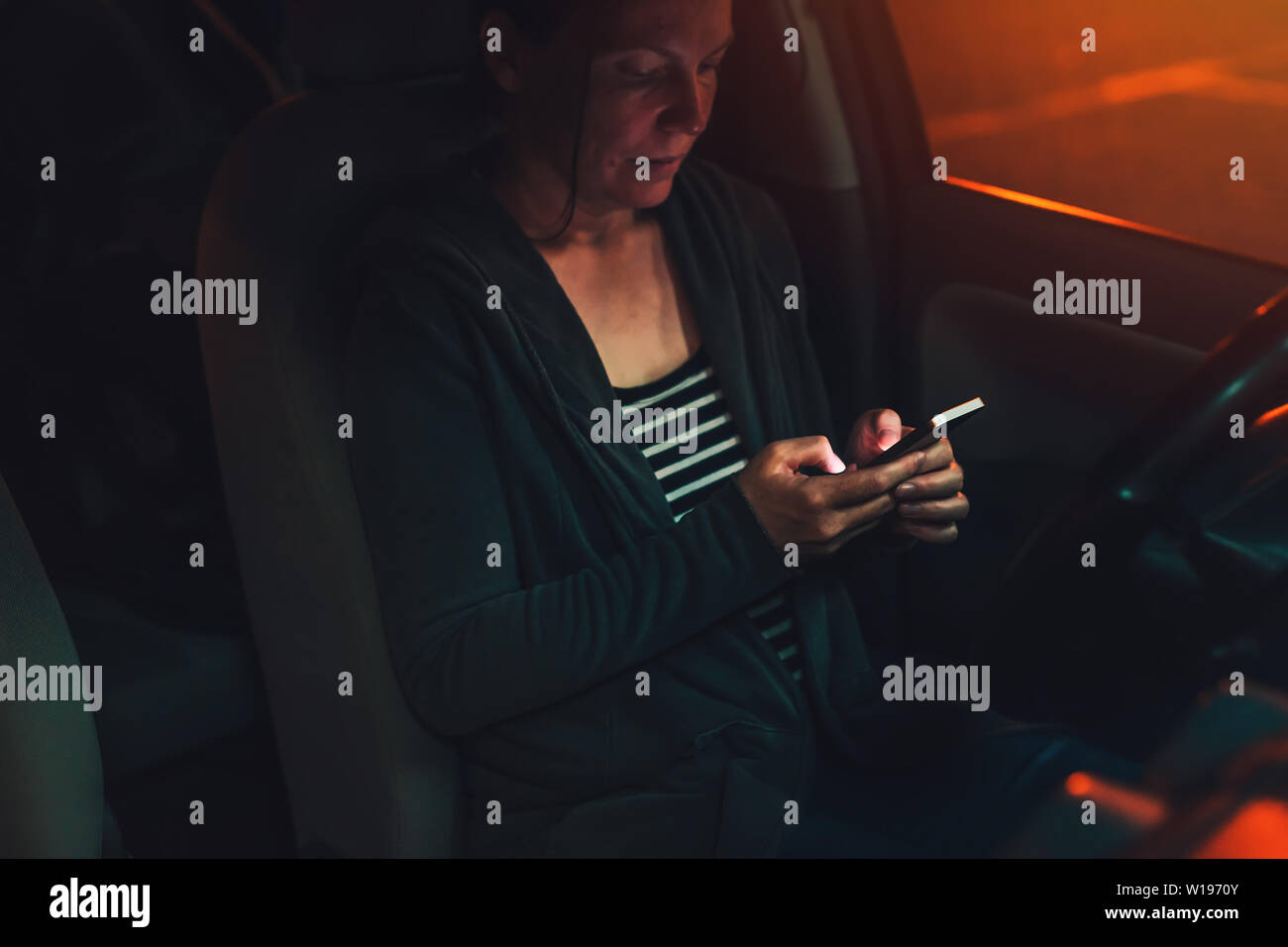 La donna gli sms su un cellulare in auto di notte in un parcheggio, femmina adulta persona utilizza lo smartphone per la comunicazione, il fuoco selettivo Foto Stock