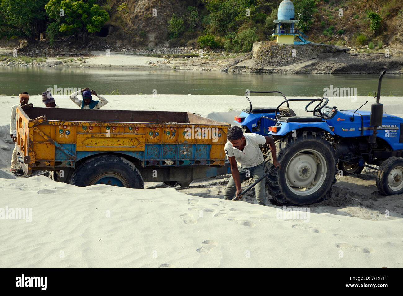 Lavoratore manuale caricamento sabbia sul trattore a riva del fiume Foto Stock