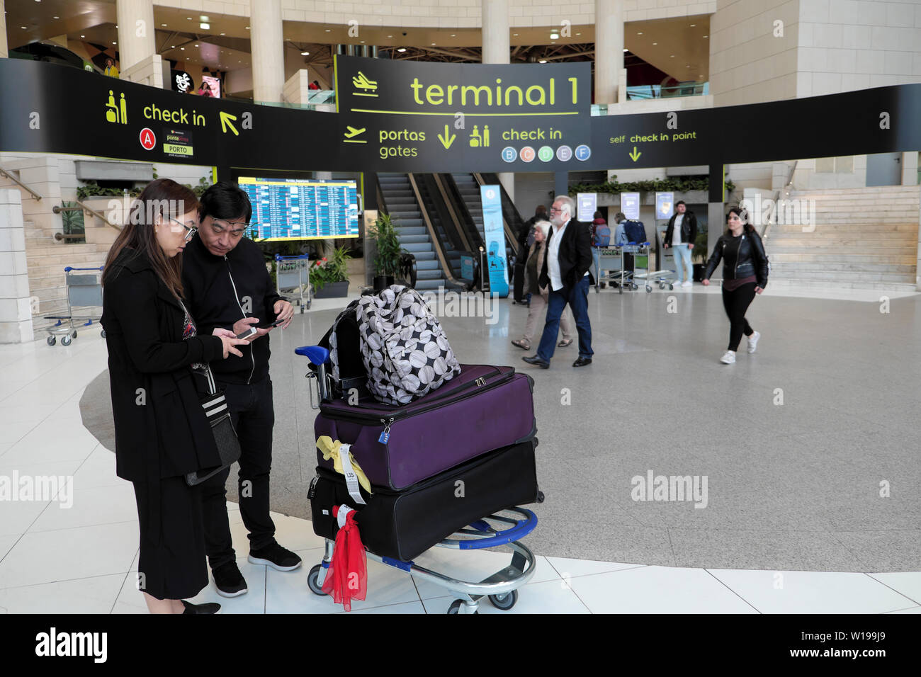 Coppia cinese con bagaglio all'interno del terminal 1 guardando i telefoni cellulari all'aeroporto di Lisbona in Portogallo Europa UE KATHY DEWITT Foto Stock