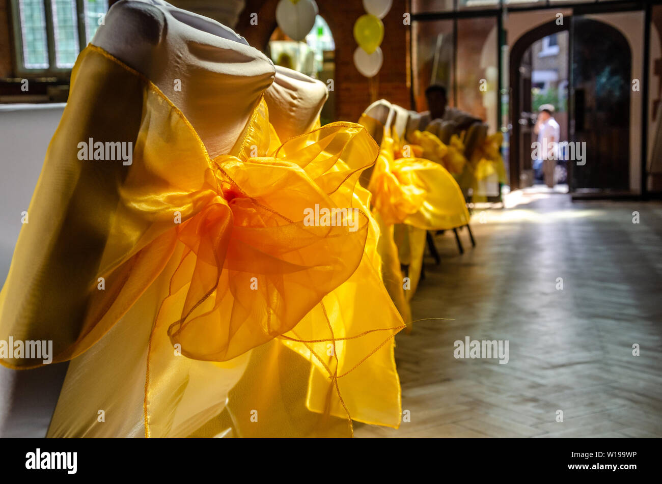 Sedie in occasione di un ricevimento in una sala vestito con tessuto bianco e decorato con nastro giallo archi. Foto Stock
