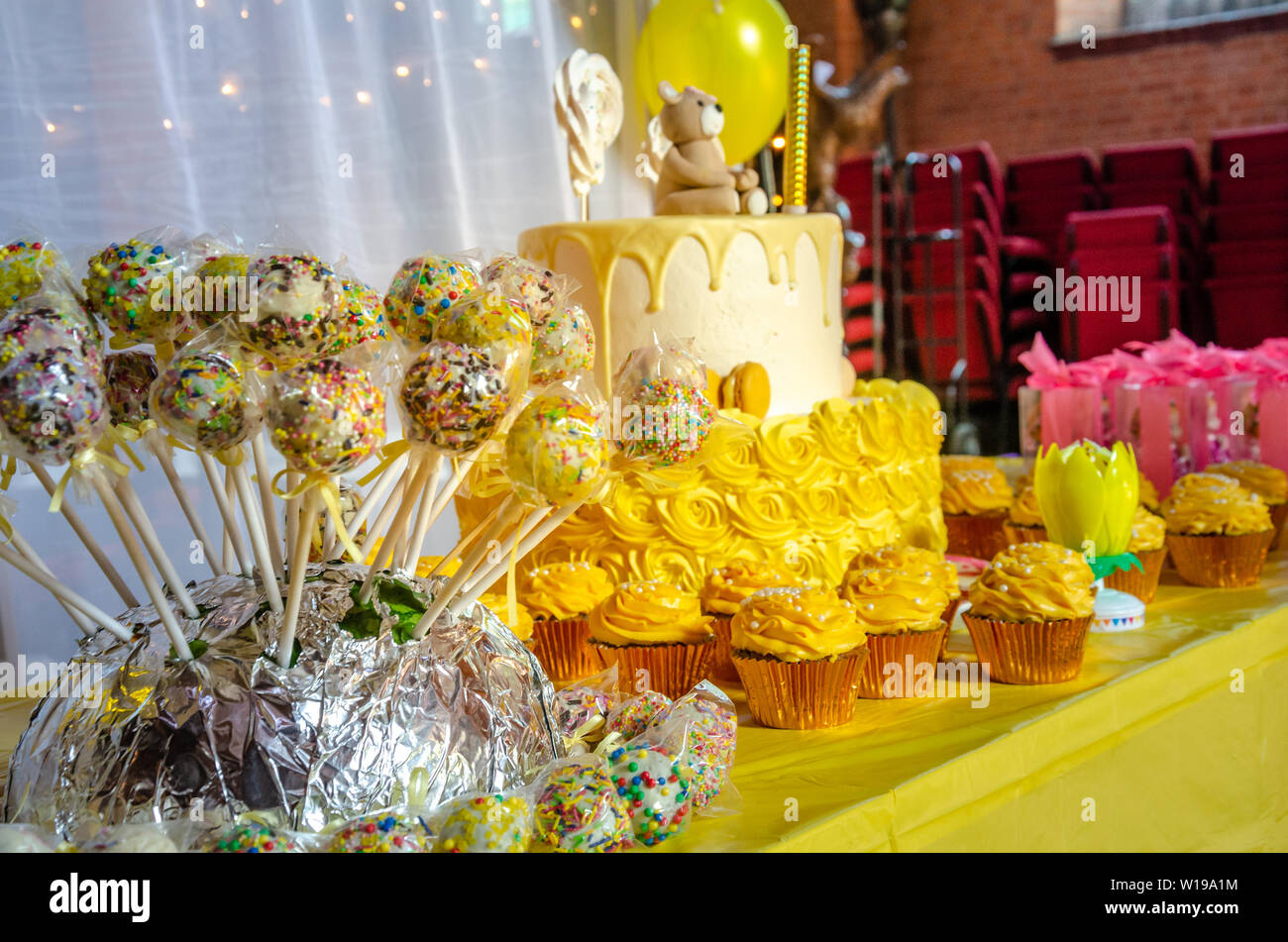 Una tabella con una torta di compleanno e tortini di giallo e una torta pop e una festa di compleanno celebrazione. Foto Stock
