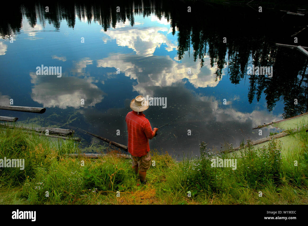 Uomo di pesca in lago di montagna con la riflessione o alberi Cielo e nubi Foto Stock