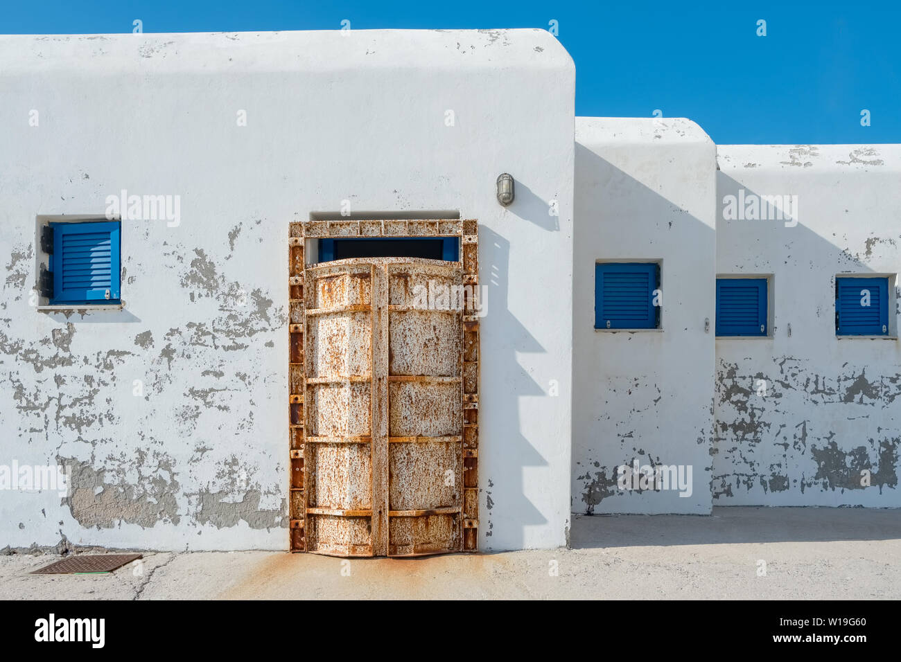 Facciata bianca del dock edificio tradizionale con finestre blu e il vecchio arrugginito porta sull'isola di Andros, Grecia Foto Stock