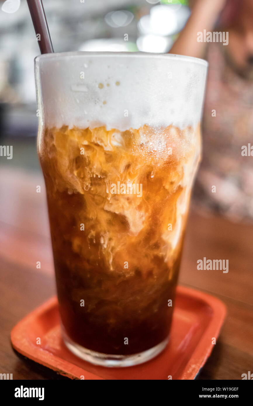 Caffè ghiacciato close-up su una tavola di legno con la crema che viene versato in esso Foto Stock