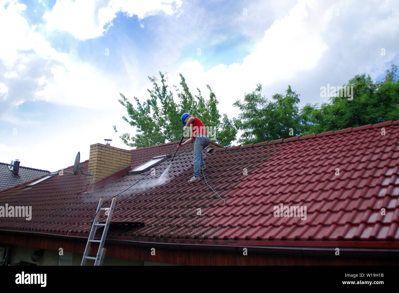 Casa la pulizia del tetto con strumento di pressione. Lavoratore sulla parte superiore dell edificio piastrella di lavaggio con attrezzature professionali. Moss rimozione con acqua. Foto Stock