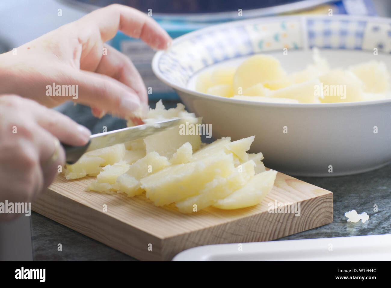 Mani tenendo un coltello tagliare alcune patate in una cucina rustica. Svuotare lo spazio di copia per l'editor di testo. Foto Stock