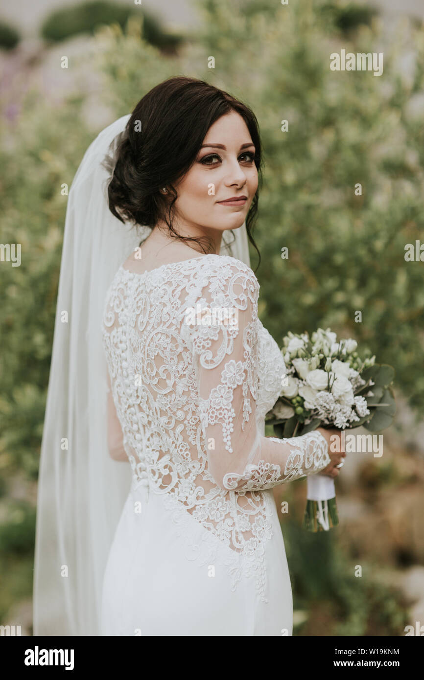 Sposa azienda Bouquet nozze. Ritratto di giovane sposa indossa lacey elegante abito da sposa guardando nella telecamera. Foto Stock