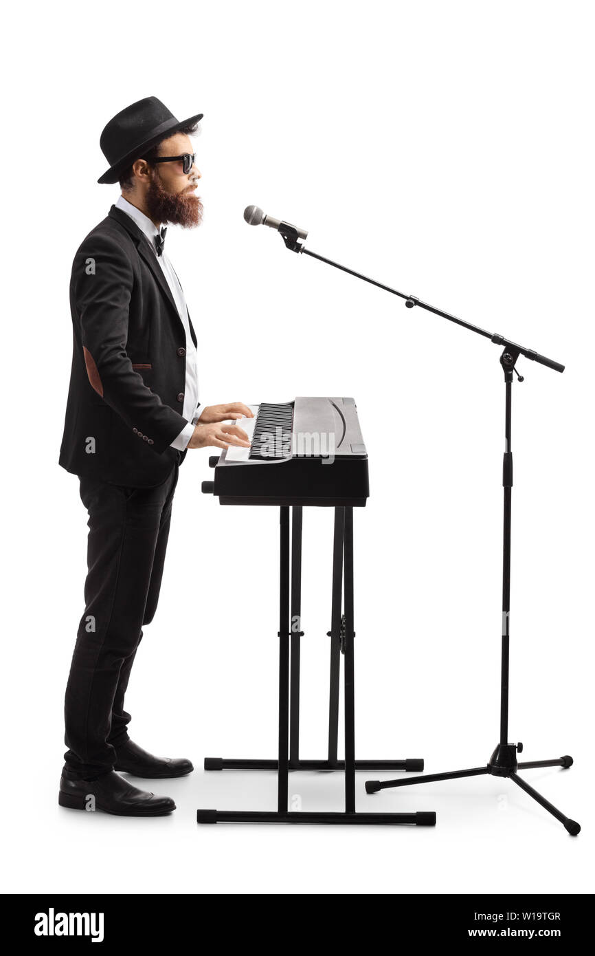 Lunghezza piena ripresa del profilo di un musicista maschio riproduzione di un pianoforte digitale e cantando su un microfono isolati su sfondo bianco Foto Stock