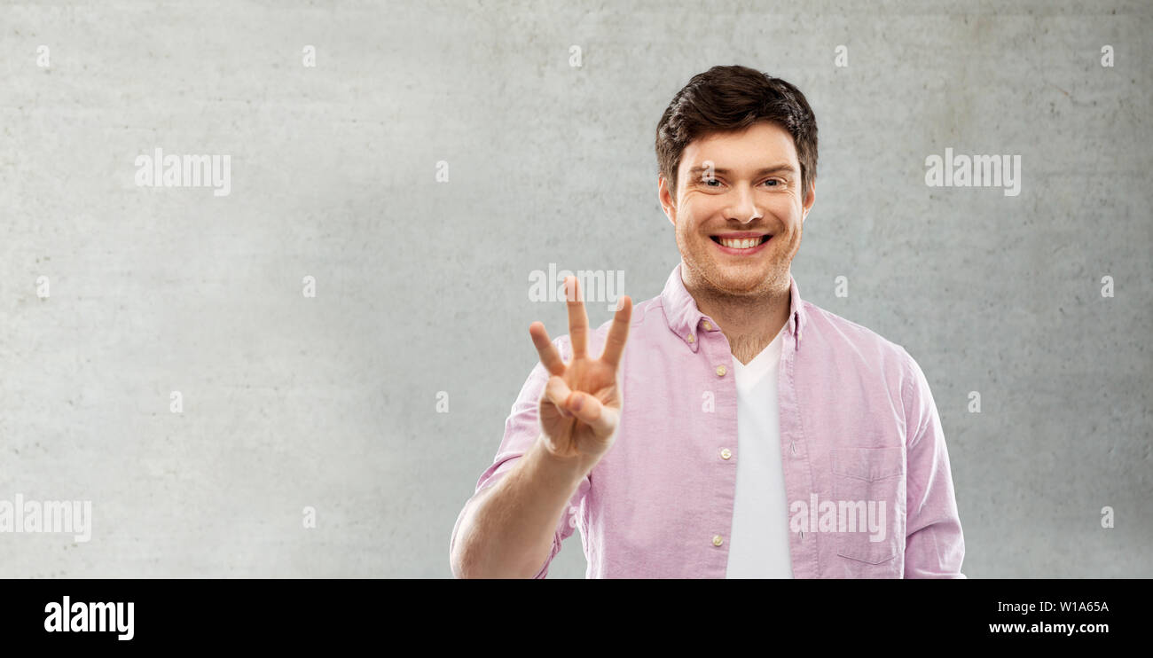 Uomo che mostra tre dita su grigio muro di cemento Foto Stock