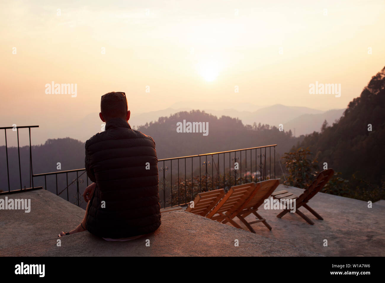 Vista posteriore del giovane uomo seduto da solo sulla parte superiore terrazza guardando le vedute panoramiche della montagna durante il tramonto. San José del Pacífico, Oaxaca, Messico. Maggio 2019 Foto Stock