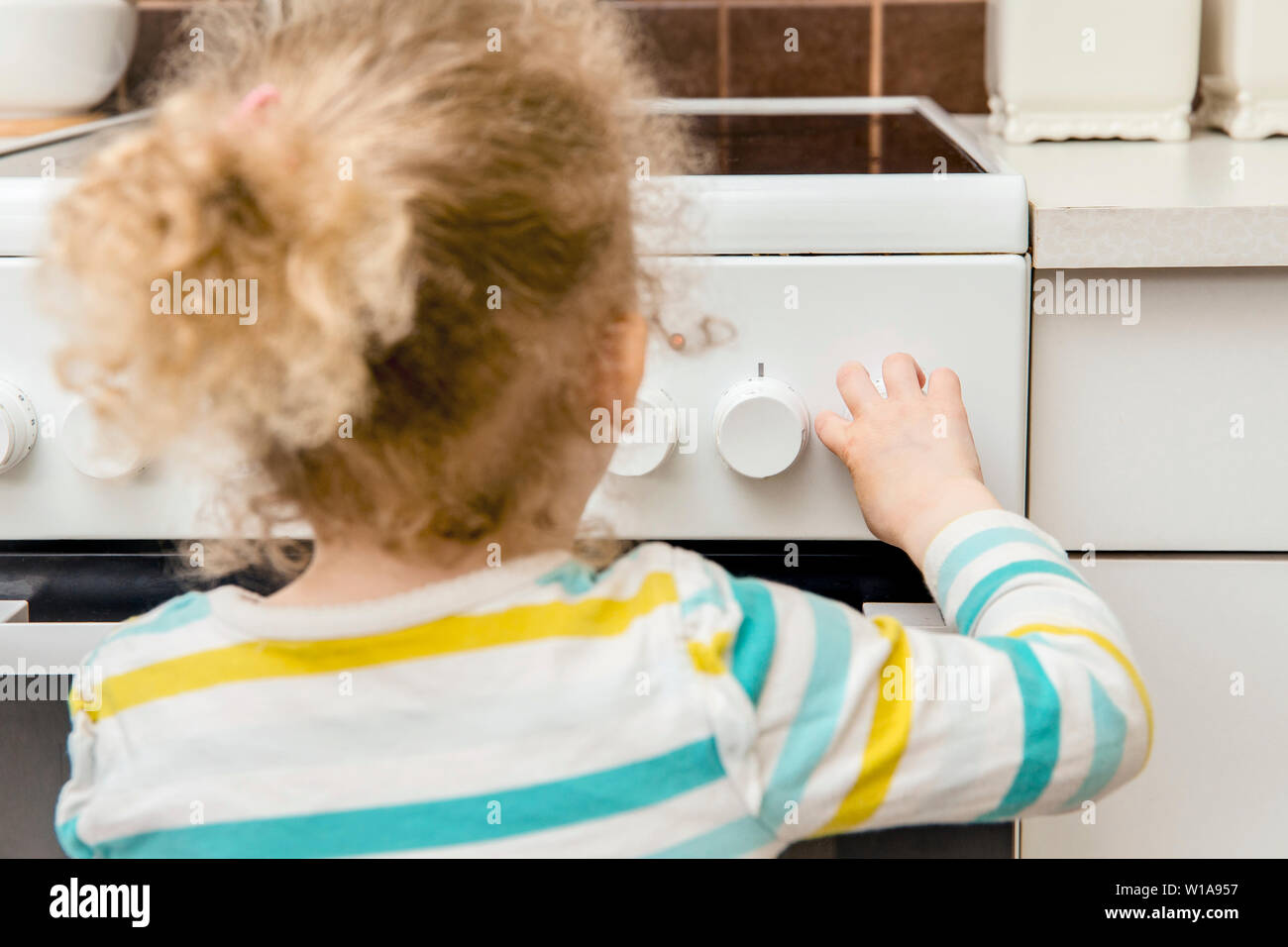 Vista ravvicinata del bambino incustodito giocando e girando fornello da cucina pomelli da soli in cucina. Pericolo di incendio nel concetto di casa. Foto Stock
