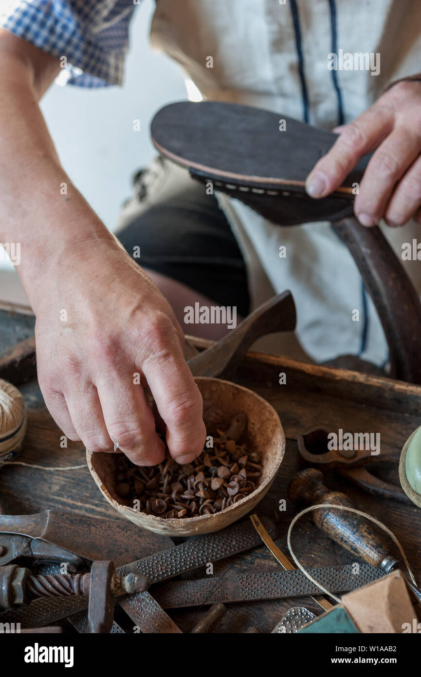 Calzolaio si applica un proiettile sulla suola di una calzatura. Vari strumenti e lo strumento sono collocati sul banco di lavoro. Foto Stock