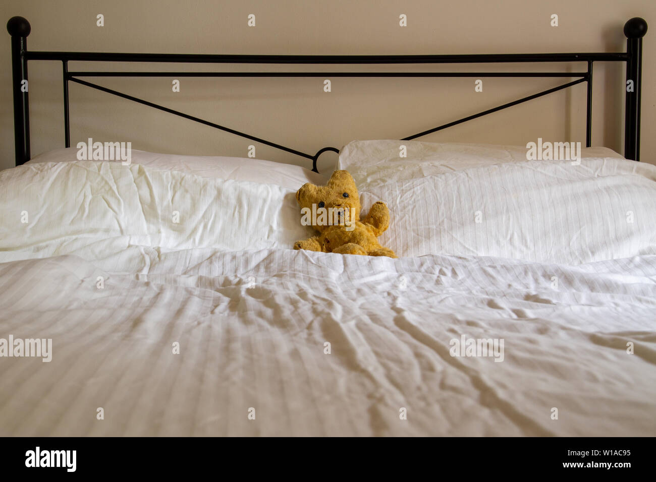 Un vecchio orsacchiotto giace su un accartocciate il piumone bianco su di  un letto doppio con
