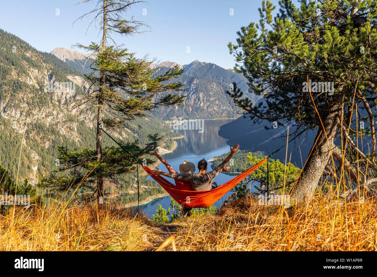 Coppia in seduta amaca con vista panoramica delle montagne e lago, lago Plansee, Ammergauer Alpi, distretto di Reutte, Tirolo, Austria Foto Stock