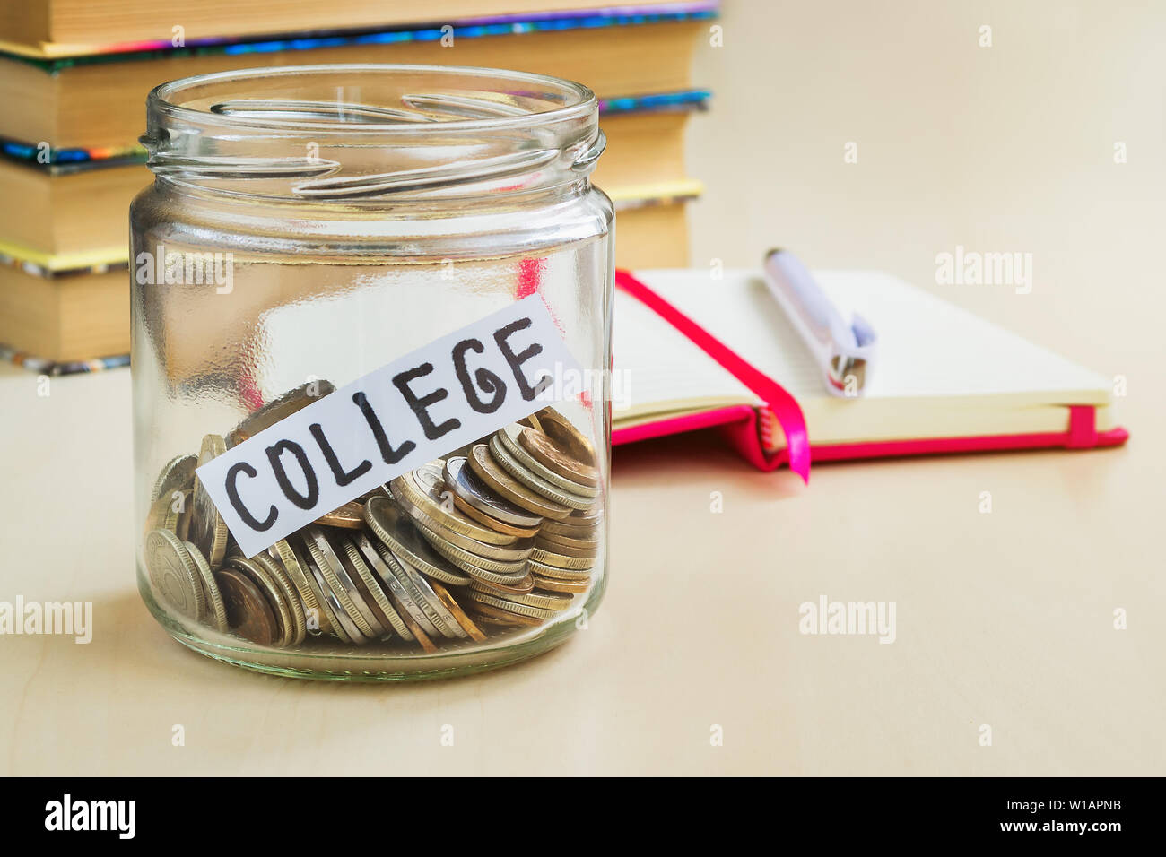 Un sacco di monete e college di parola in un vasetto di vetro nei pressi di un bianco con penna a sfera e alcuni libri su un tavolo. Risparmio di denaro per il college e il concetto di istruzione. Pl Foto Stock