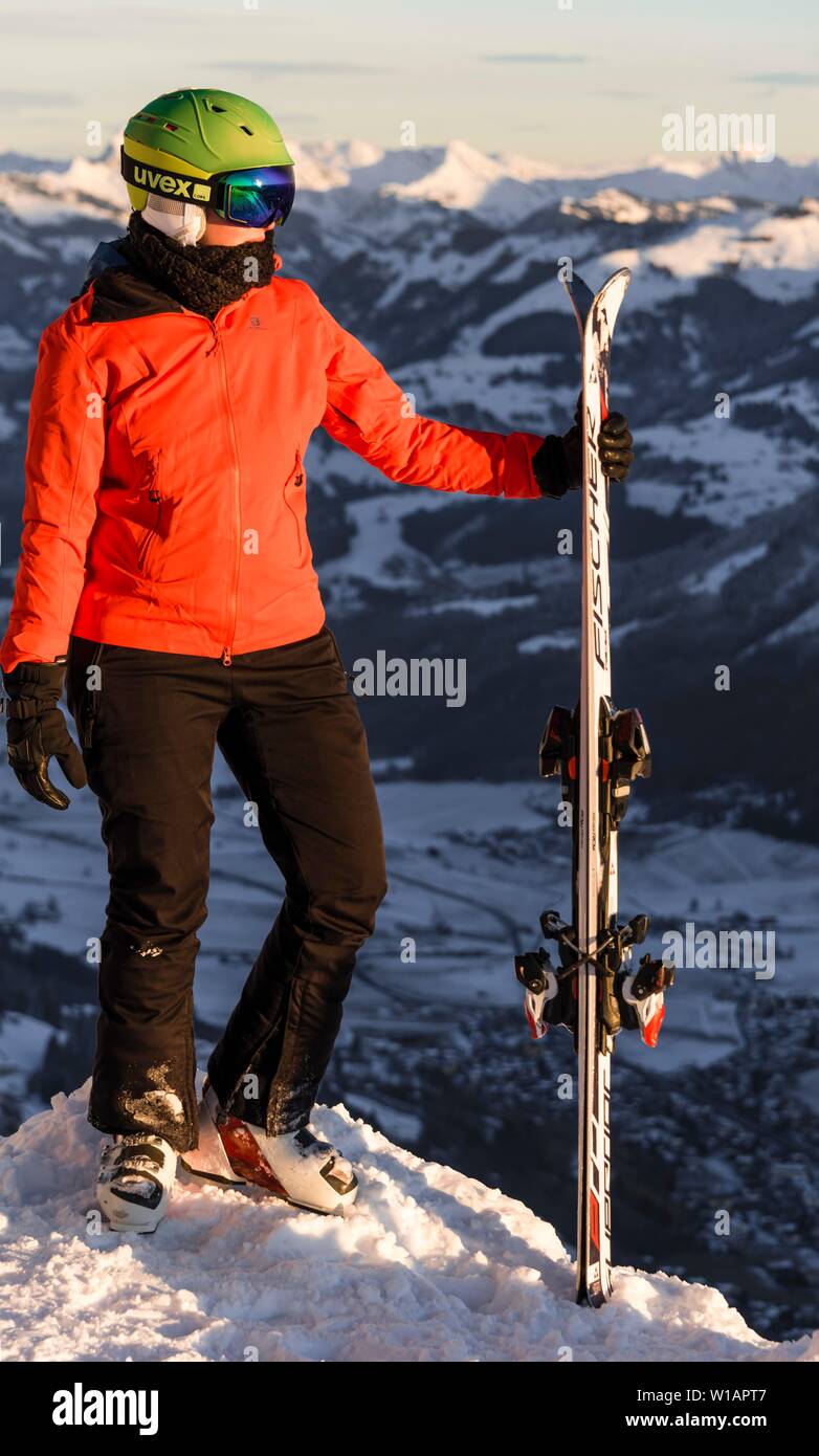 Sciatore femmina con casco da sci in piedi con sci presso la pista da sci al di sopra della valle, guardando al lato, montagne dietro, SkiWelt Wilder Kaiser Foto Stock