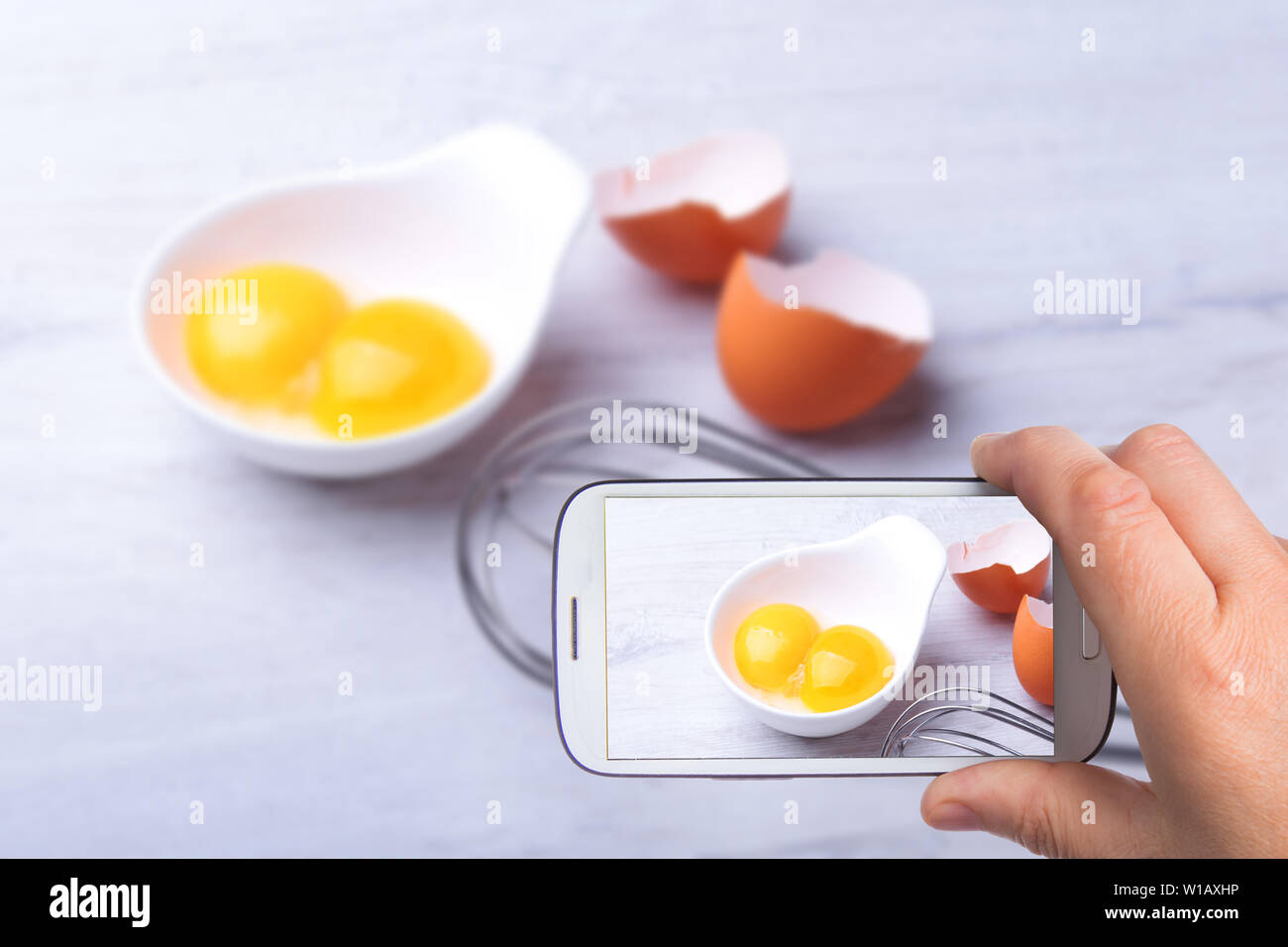 Le mani di uomo con lo smartphone tenendo photo tuorlo d'uovo. ingrediente per il tiramisù fatti in casa torta in close up. Foto Stock