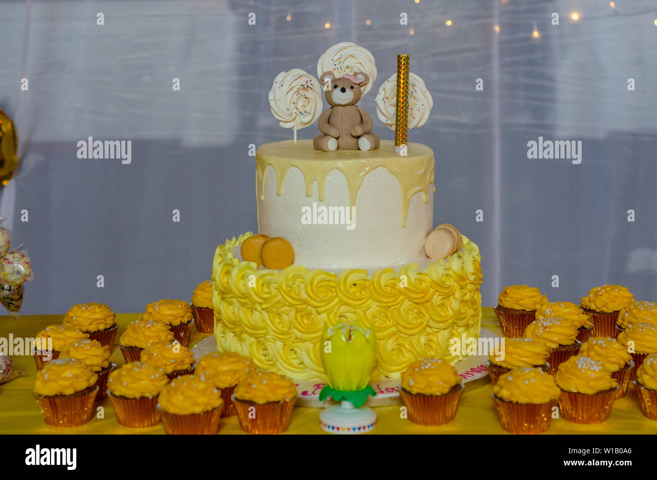 Un due tier torta di compleanno circondato da tortini di giallo su un tavolo. Foto Stock