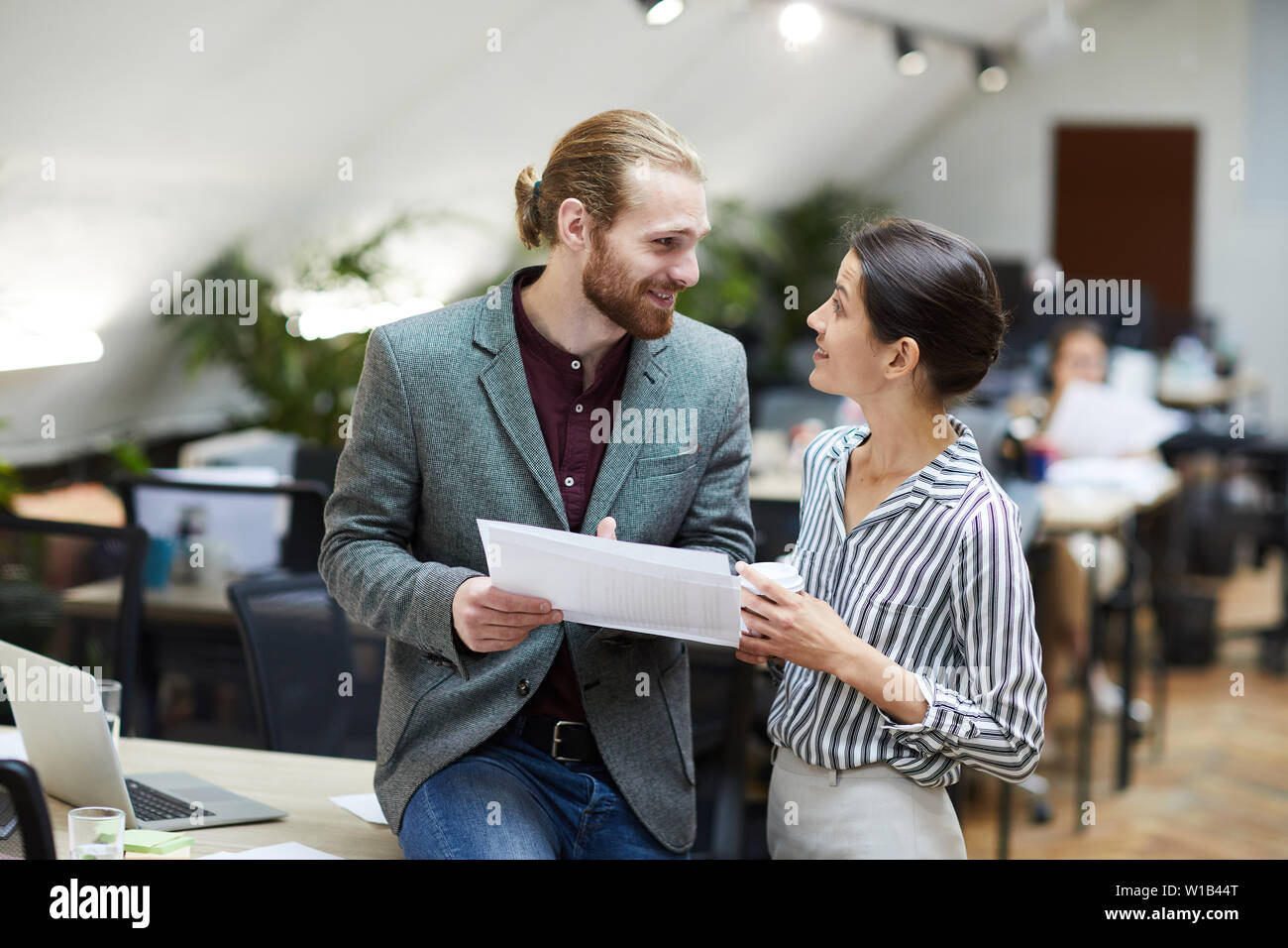 Vista laterale ritratto di imprenditore bello sorridente al collega femmina chiacchierando in ufficio, spazio di copia Foto Stock