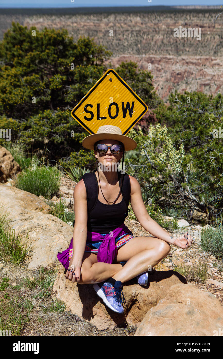 Donna seduta in un yoga pone vicino un segno lento nel South Rim, il Parco Nazionale del Grand Canyon, Arizona, Stati Uniti d'America Foto Stock