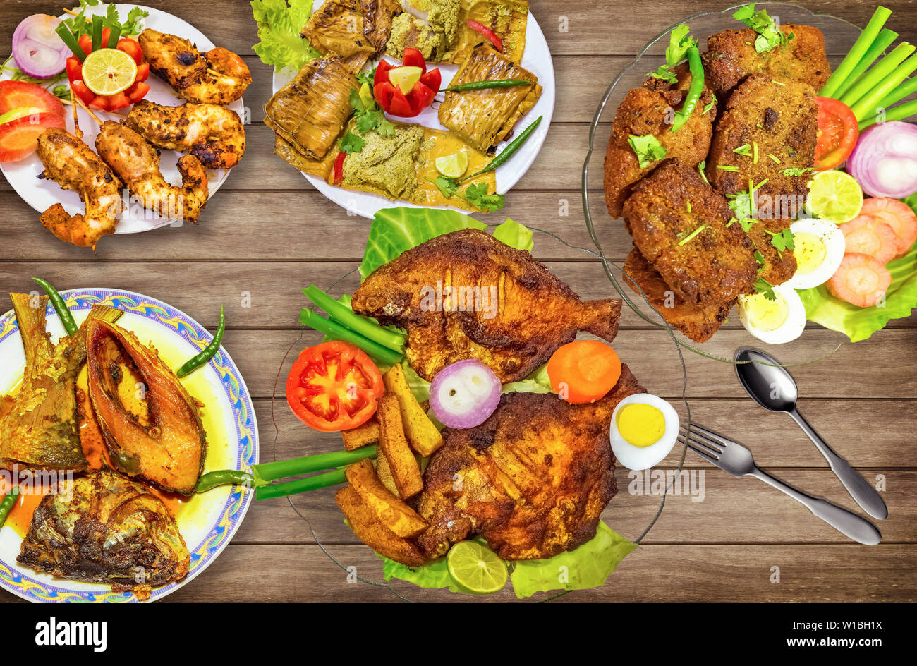 Indian pesci piatti comprendente di fritte pomfret pesce con hilsa olio di pesce al curry e fritti croccanti di gamberi con insalata mista su tavola di legno Foto Stock