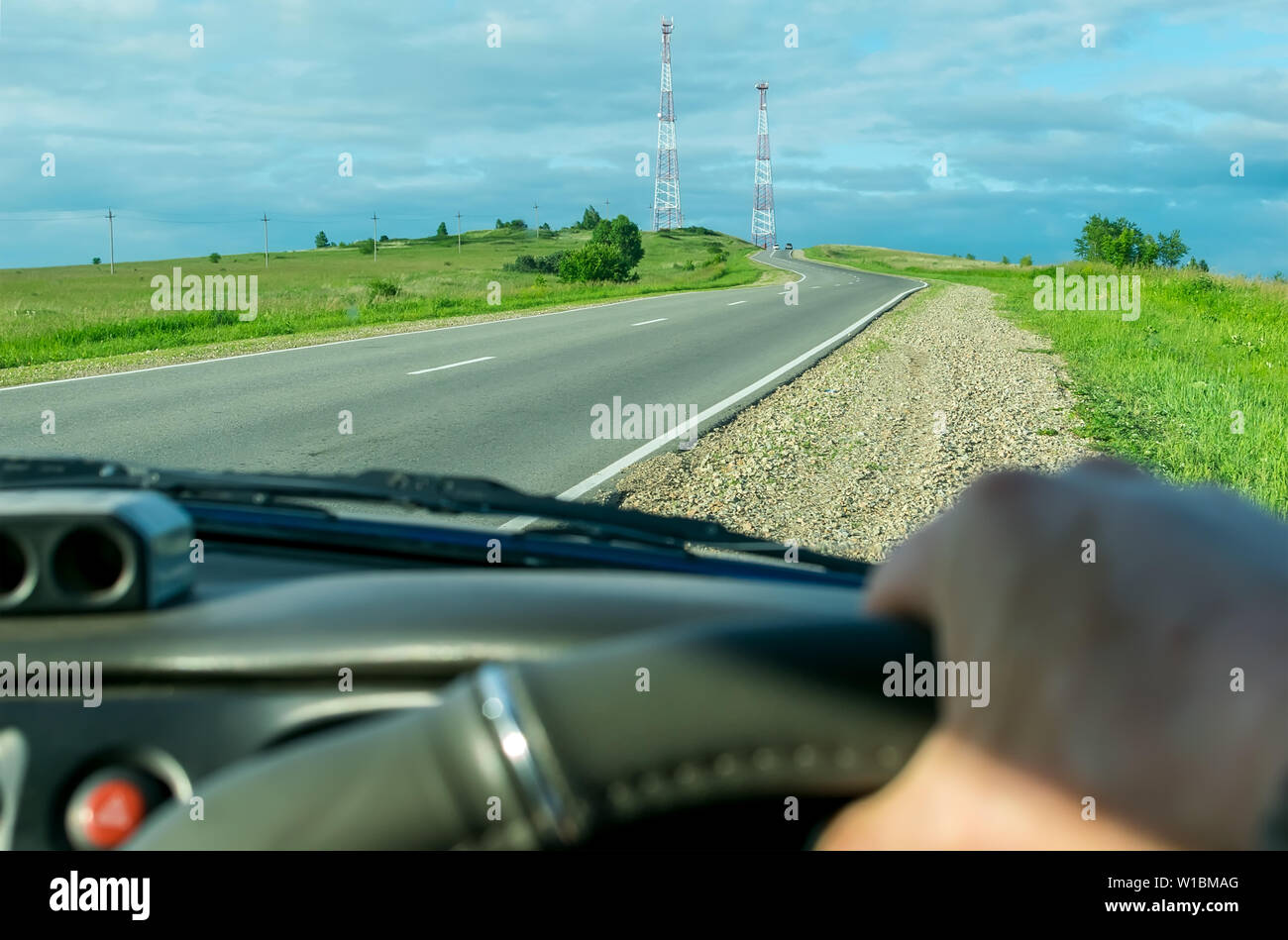 Vista dal lato del conducente della vettura le mani sul volante di sterzo sullo sfondo del paesaggio e salendo su per la collina strada con torri radio Foto Stock