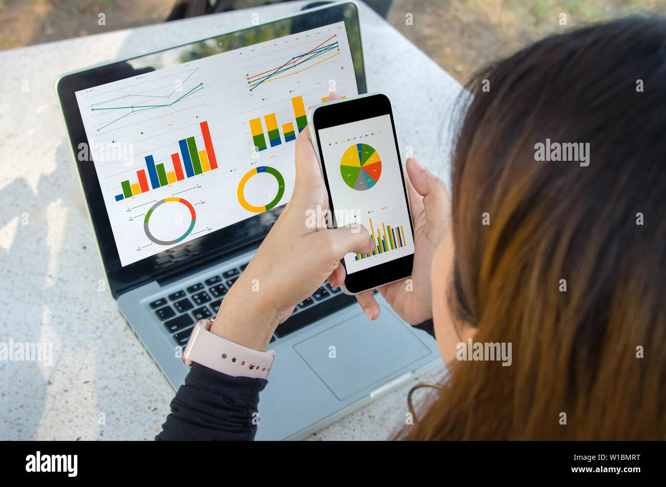 Imprenditrice lavorano seduti all'aperto il laptop e smartphone con grafici, diagrammi e grafici sullo schermo. Foto Stock