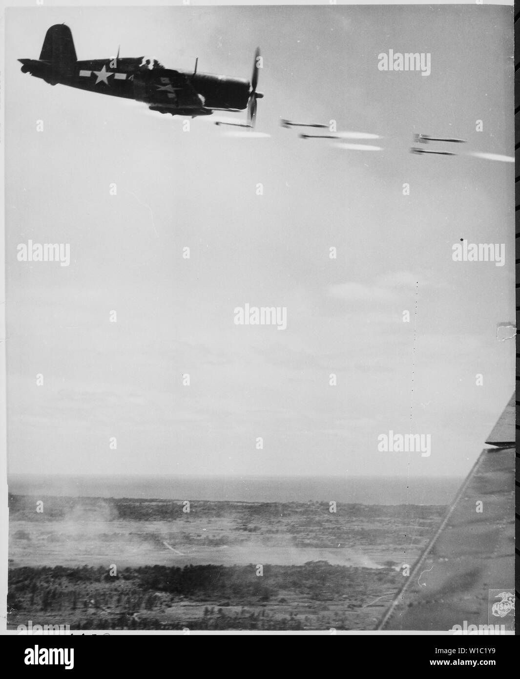 Corsair fighter perde il suo carico di proiettili a razzo su una corsa contro una roccaforte Jap su Okinawa. Nella parte inferiore di sfondo è il fumo della battaglia come le unità marine si muovano per seguire con un punzone di domenica, ca. 06/1945 Foto Stock