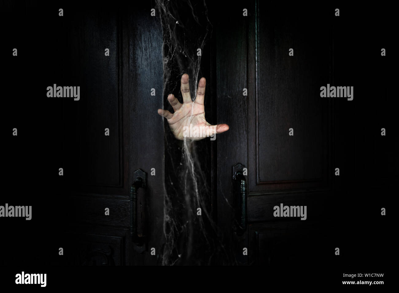 La mano dell'uomo con il bastone dalla porta di legno dall'interno della camera oscura Foto Stock