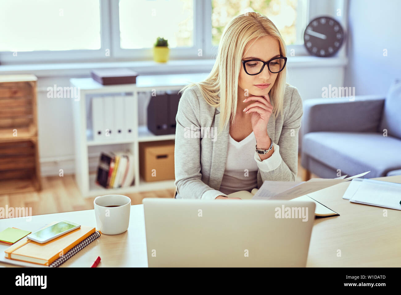 Premurosa donna financail lettura di documenti mentre si lavora con il computer portatile dalla sua home office Foto Stock