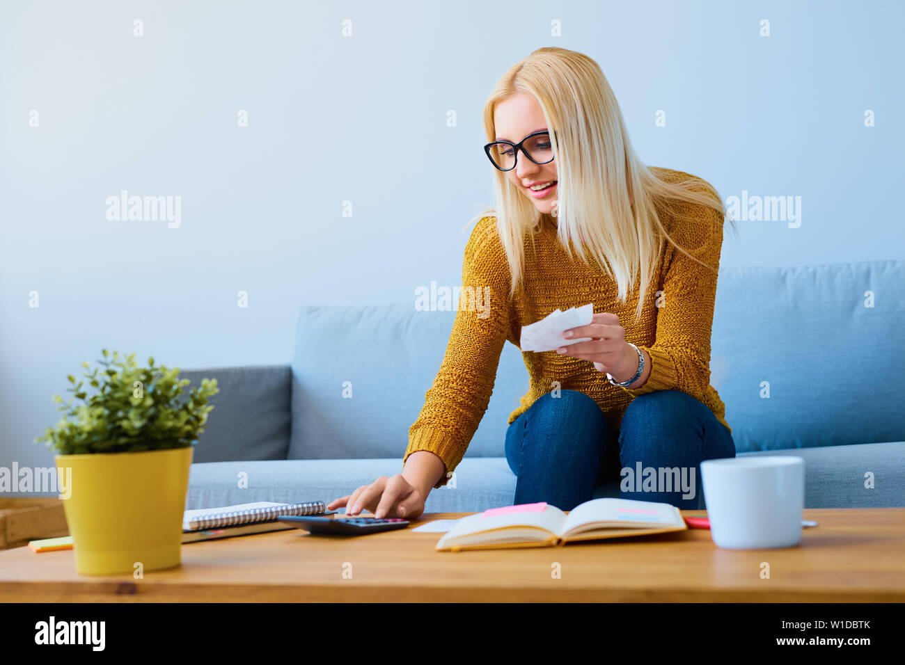 Giovane donna con cambiali calcolo delle finanze, seduto sul divano Foto Stock