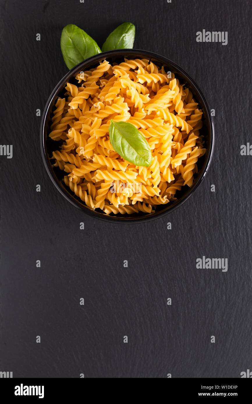 Concetto di alimentare di materie organiche Fusili italiana la pasta nella ciotola nero su nero ardesia scheda con spazio di copia Foto Stock