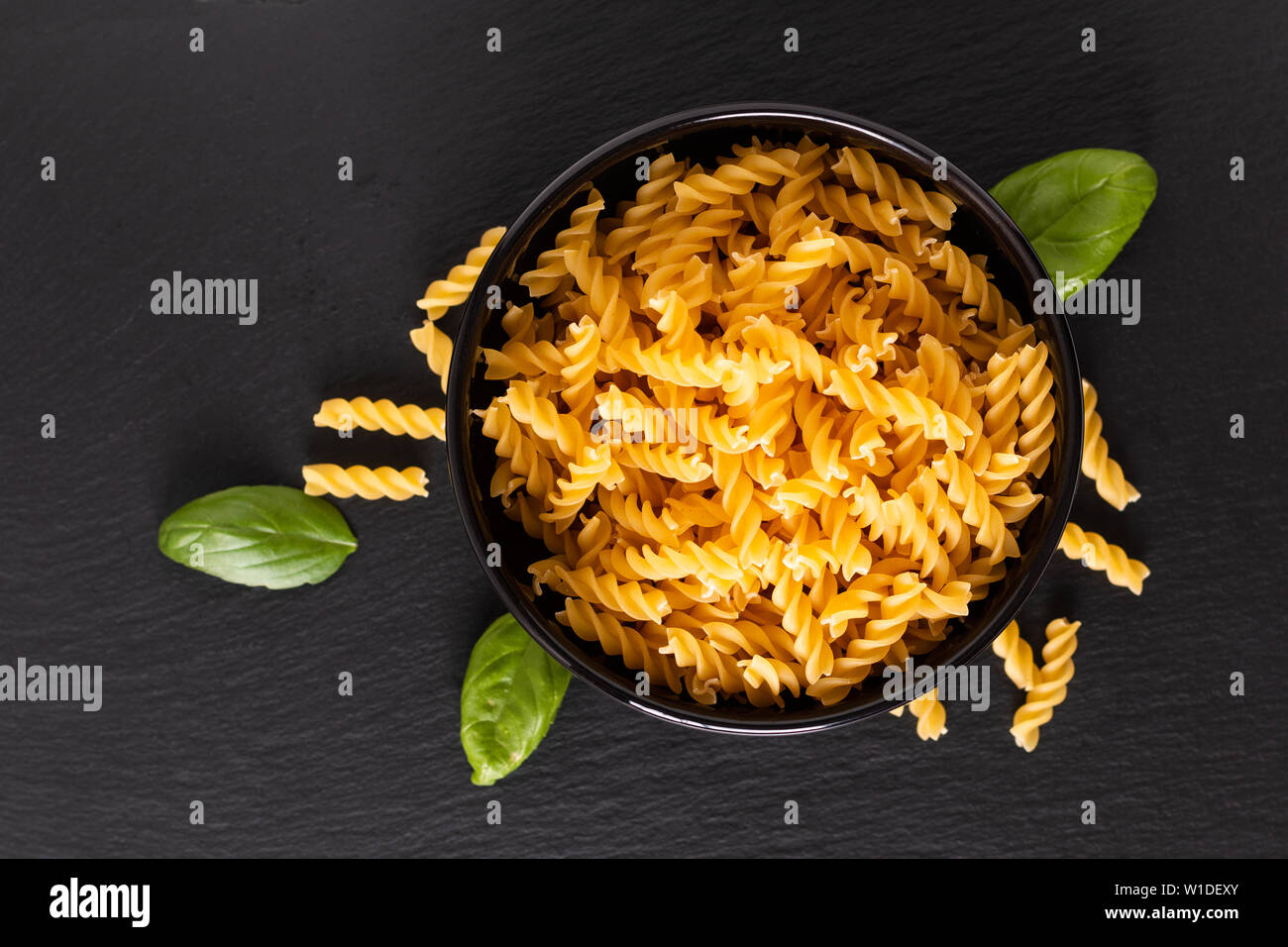 Concetto di alimentare di materie organiche Fusili italiana la pasta nella ciotola nero su nero ardesia scheda con spazio di copia Foto Stock