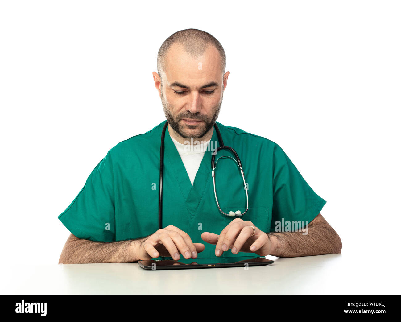Medico con abiti verdi utilizza un tablet seduti ad un tavolo isolato su bianco. La tecnologia utilizzata nelle attività mediche. Foto Stock