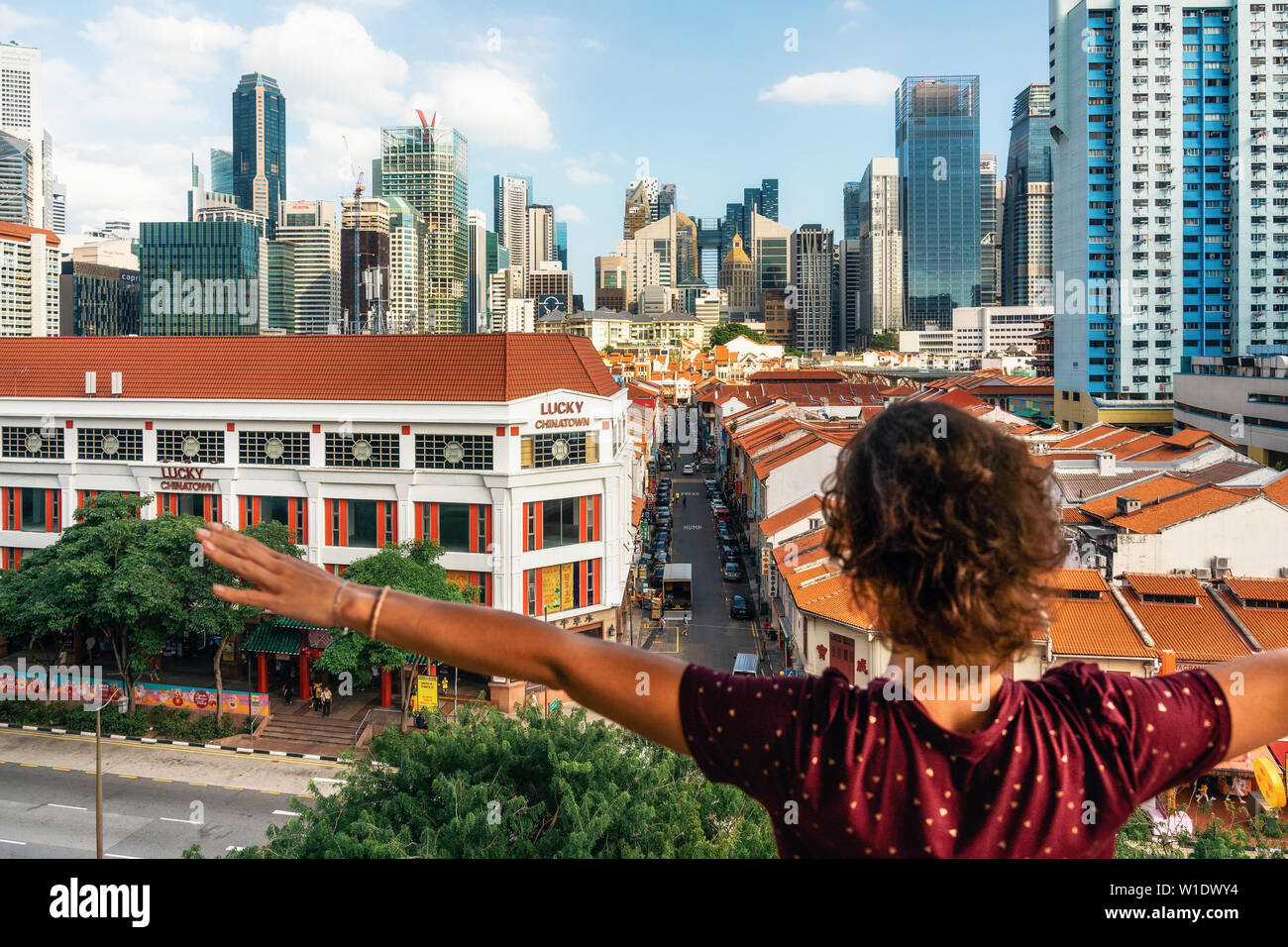 Chinatown, Singapore - 8 Febbraio 2019: giovane donna felice sorge torna alla telecamera con le mani alzate e gode di vista aerea di Chinatown con tetti rossi Foto Stock