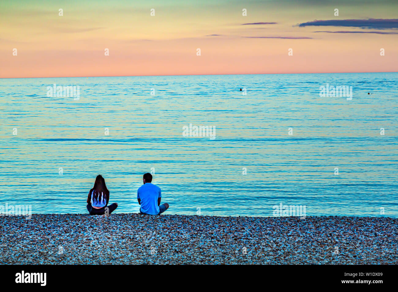 Una giovane coppia sedersi sulla spiaggia al tramonto in un molto romantica scena. Foto Stock